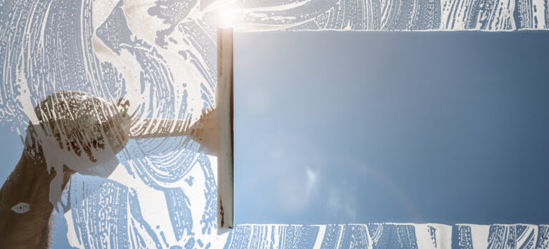 Window cleaner using a squeegee to wash a window with clear blue sky