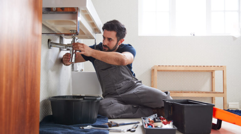 Male Plumber Working To Fix Leaking Sink In Home Bathroom